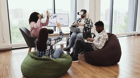 Young adults engage with virtual reality devices and laptops in collaborative office. Diverse teams demonstrating technology interaction seated on floor and chairs creating innovative atmosphere. - Powered by Shutterstock - Get 15% off with code: PIKWIZARD15