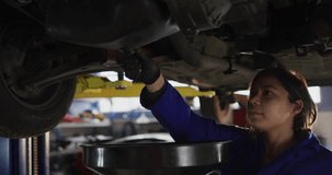 Female mechanic aligning drain pan under vehicle on lift and initiating oil drain for maintenance. Automotive, repair, industry, mechanic, tools, mechanicwear, servicebay - Powered by Shutterstock - Get 15% off with code: PIKWIZARD15