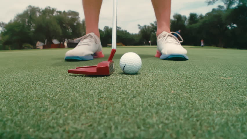 Extreme slow-motion close-up of golfer’s feet and putter taking back and striking ball. Highlights precision, stance, technique, and short game control