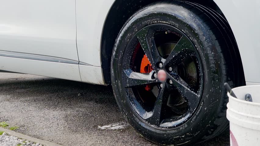 Spraying foam cleaner onto blac alloy wheels and tyres on white SYV