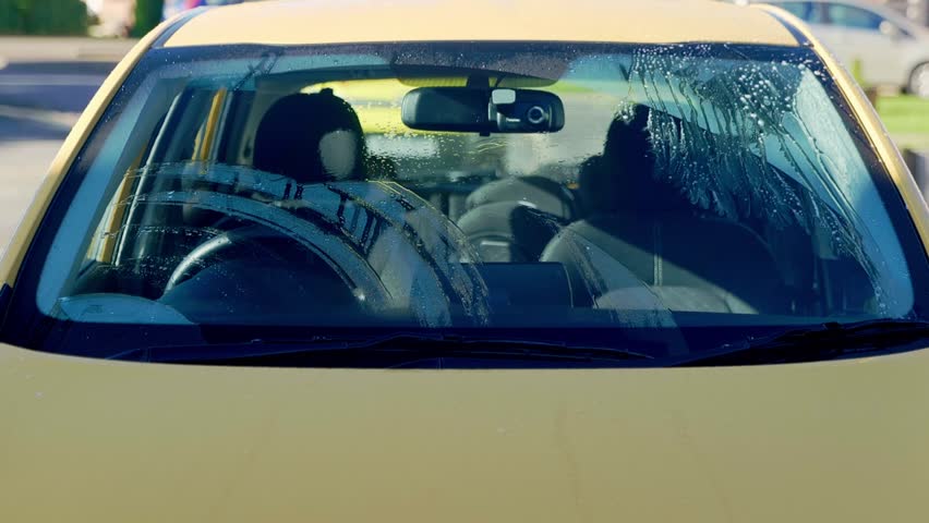 Washing yellow car windscreen with blue mitt and lots of shampoo suds