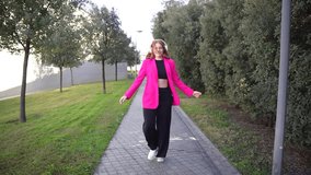 A fashionable woman in a chic pink blazer and stylish black pants strolls along a scenic pathway lined with trees, proudly showcasing her vibrant style in this serene outdoor setting - Powered by Shutterstock - Get 15% off with code: PIKWIZARD15