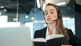 Portrait of businesswoman, wearing a headset and business attire, works diligently with a laptop and notebook in a modern office, focused on online communication, appearing serious. - Powered by Shutterstock - Get 15% off with code: PIKWIZARD15