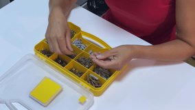 A person carefully selects screws from a yellow partitioned hardware organizer on a white table. This focused action shows preparation for a home repair or assembly task - Powered by Shutterstock - Get 15% off with code: PIKWIZARD15