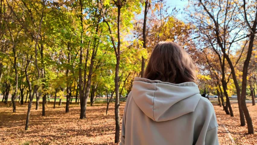 Slow motion picture of a sad woman walking along a path in an autumn park.