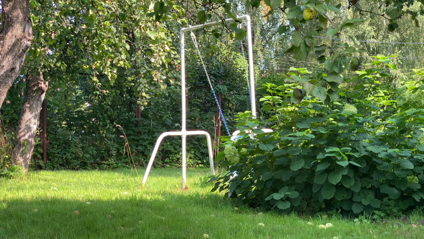A child in blue joyfully swings in a vibrant green garden, surrounded by trees and bushes. The scene captures a happy and active moment of outdoor play on a sunny day.