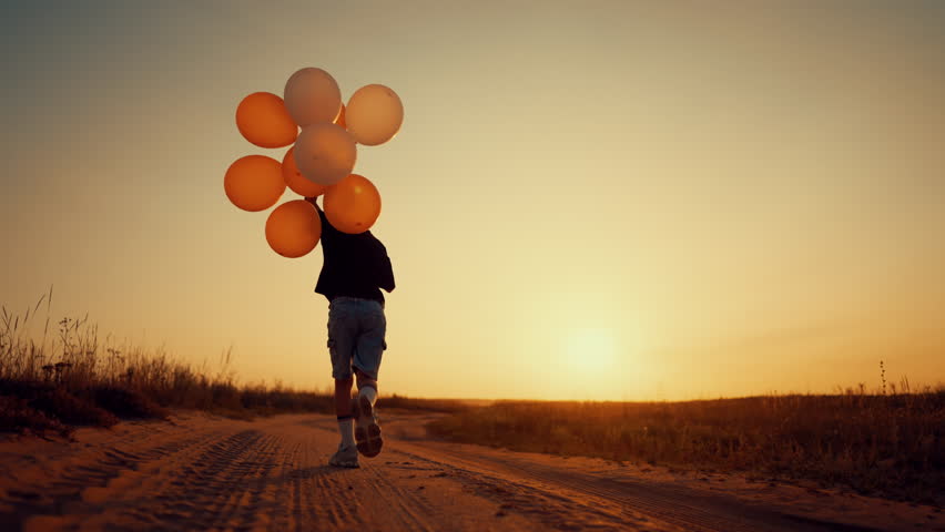 Lonely child with balloons in hand running in desert in sunset, back view. Childhood moments, move to dream and be yourself, little dreamer moving forward, cinematic slow motion shot, kid in nature