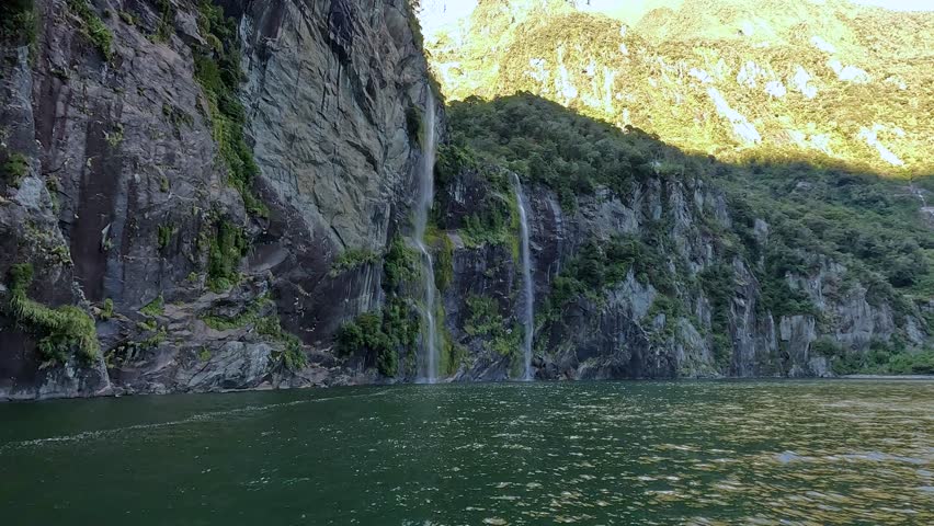 View from a boat sailing towards twin waterfalls cascading down a mountain in Milford Sound in the Fiordland National Park, New Zealand. This is a popular tourist destination in the South Island.