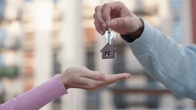 Vertical close up of hands, male real estate agent handing over house key with home shaped keychain to young woman in front of modern apartment building. Concept of real estate deal, housing service. - Powered by Shutterstock - Get 15% off with code: PIKWIZARD15