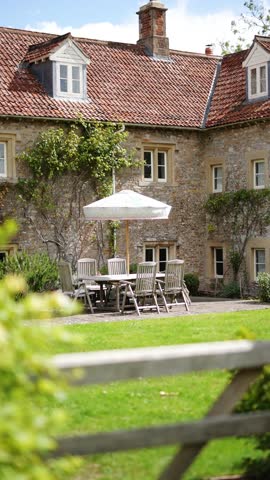 A large stone house with a white umbrella on the front lawn. The house has a lot of windows and a white awning