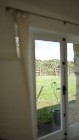 A window with a white curtain and a view of a field. The curtain is open, letting in the light and the view of the field