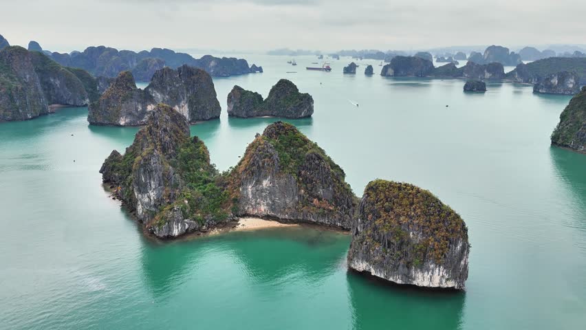 Turquoise waters surround towering limestone islands in Ha Long Bay, Vietnam, flying over scattered beaches