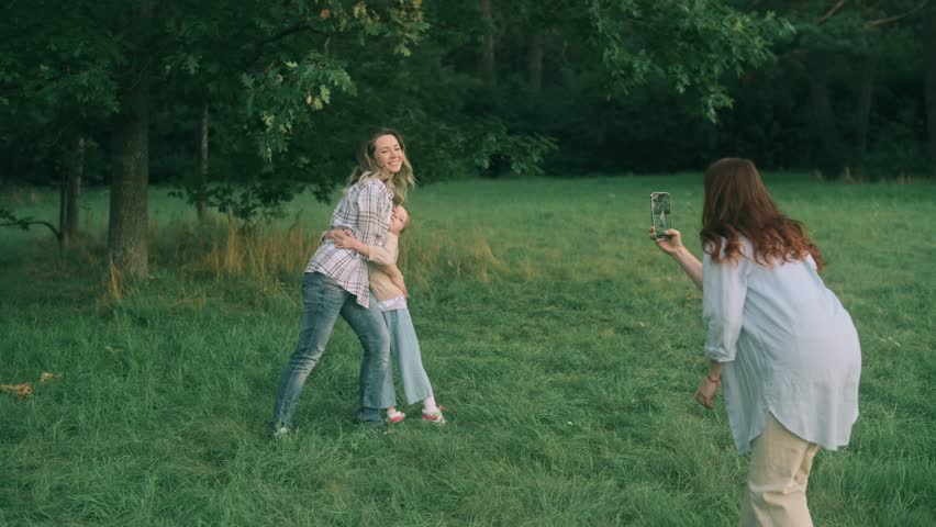 Friends are walking in nature. Two women and a child are taking pictures in park.
