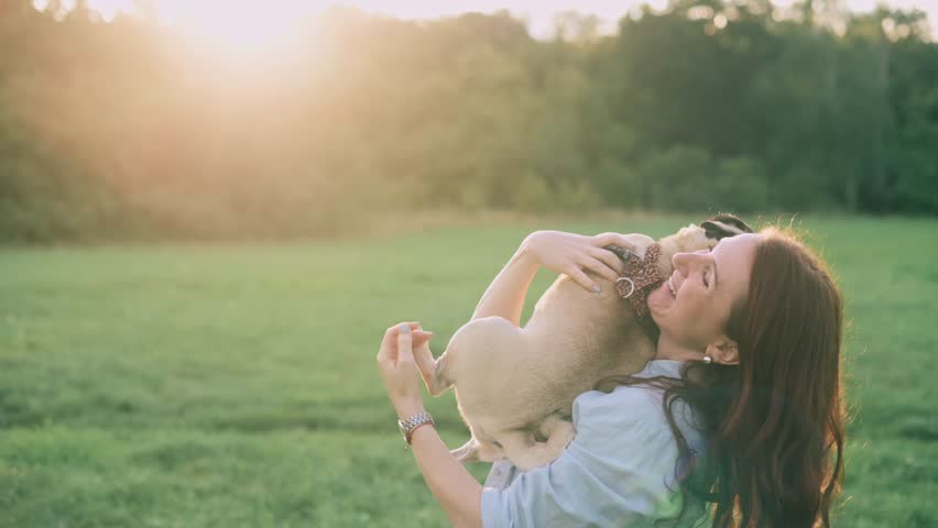 A young woman strokes and hugs her beloved pug dog outdoors.