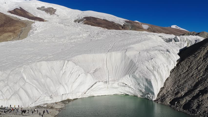 Aerial view of the stark white Muztagh Glacier meeting a turquoise glacial lake, creating a stunning contrast against the rugged terrain, Muztagh Glacier, China.