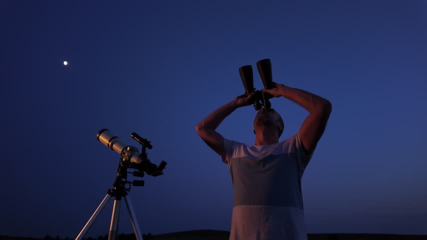 Amateur astronomer using telescope for watching stars, Moon, planets and other celestial objects from a field in nature.