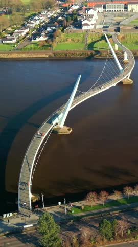 Wide reversing social ratio aerial of the Peace Bridge over the River Foyle in Derry, AKA Londonderry in Northern Ireland. Filmed in 1080x1920, 60FPS and with Rec709 color.
