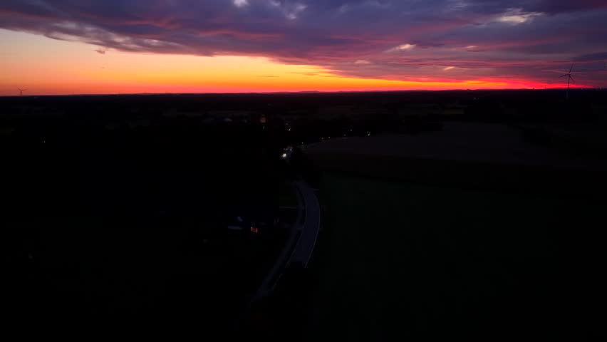 Aerial view of a dramatic sunset with glowing orange and purple sky over a rural landscape, creating a cinematic evening atmosphere. Traffic scene with cars on road. Dusk scene in usa. Wide shot.
