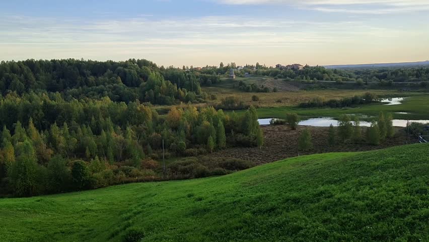 Scenic view of rural landscape with rolling hills, lakes, green fields, and forest in background. Clear sky adds to tranquil atmosphere of this picturesque countryside scene. Nature and travel 