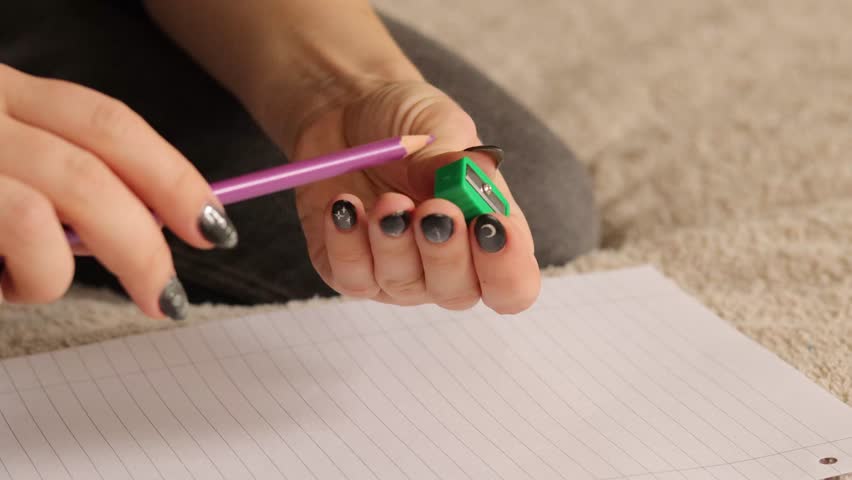 A person demonstrates sharpening a purple pencil using a green sharpener on a sheet of paper. The focus is on the neat results of this essential writing tool