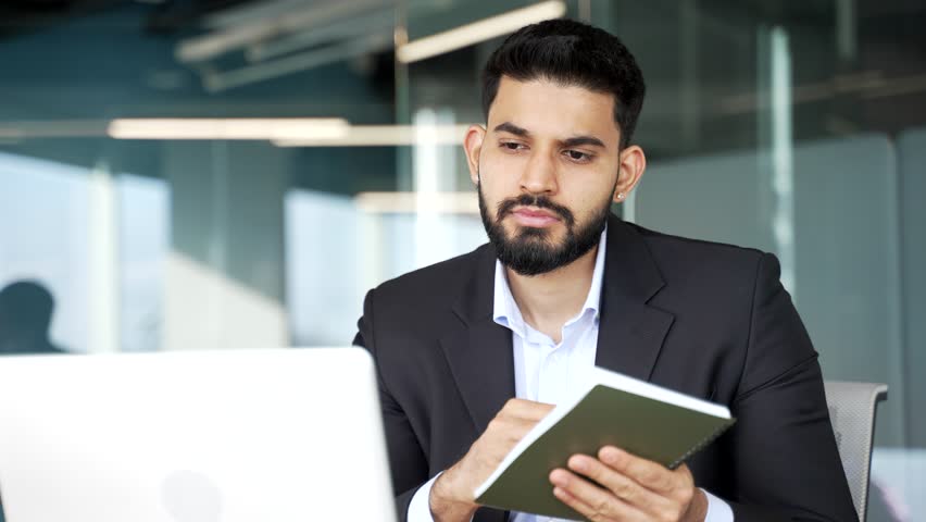 Businessman watching video call conference or training notes in notebook looking at laptop screen sitting at workplace in business office. Manager in formal suit communicates remotely online. Close up