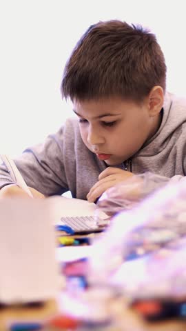 The boy of 10 years, draws a drawing, a project of a robot model, a machine, plays in the designer from cubes, plates, circuits, wires. he is fond of robotics, programming, modeling,