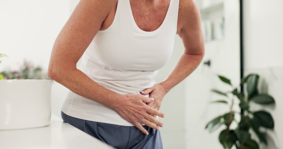 Hands, mature woman and stomach ache in home, menopause and health problem in bathroom. Constipation, discomfort and person with pain, abdomen cramps and sick with diarrhea in morning in house