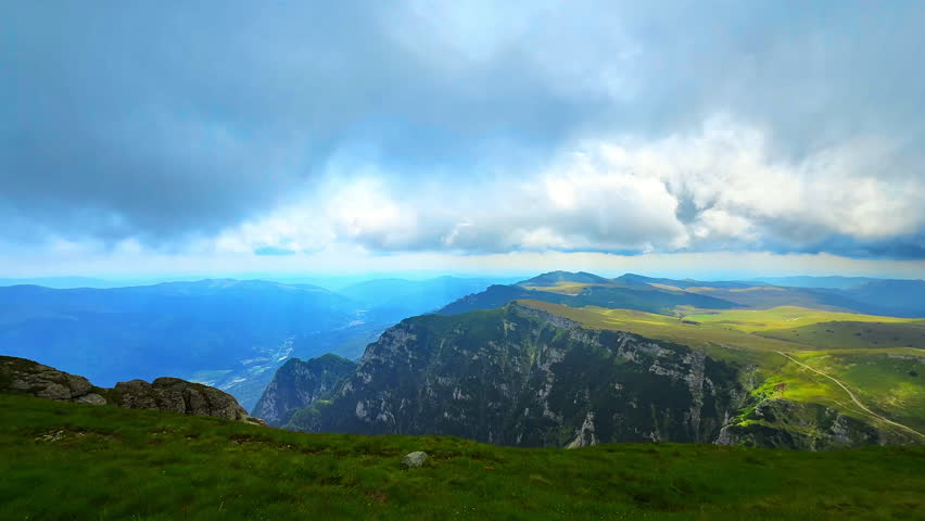 Steep cliffs and sunlit slopes in dramatic mountain scene in Romania. Scattered rocks and grassy foreground with texture and depth.