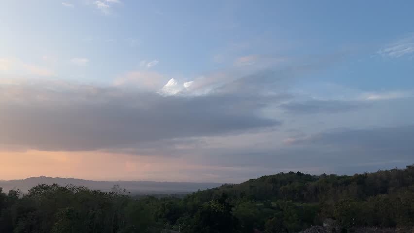 Beautiful twilight sky over tropical hills with soft orange and blue tones, creating a calm evening landscape.