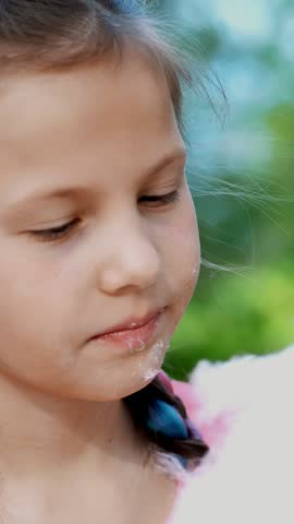 Portrait, pretty girl of eight years, blonde, with freckles, and multi-colored pigtails, eats sweet white cotton, cotton candy, candyfloss. having fun, in the city park, in summer