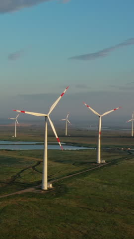 Beautiful aerial sunset landscape with lake and windmills or wind turbine on wind farm in rotation to generate electricity energy. Vertical video