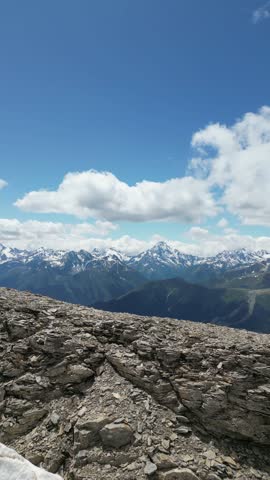Tourists at the top of the mountain range are surrounded by the Arkhyz mountains, shrouded in snow and melting glaciers. Below, there are views of green meadows and snow caps above