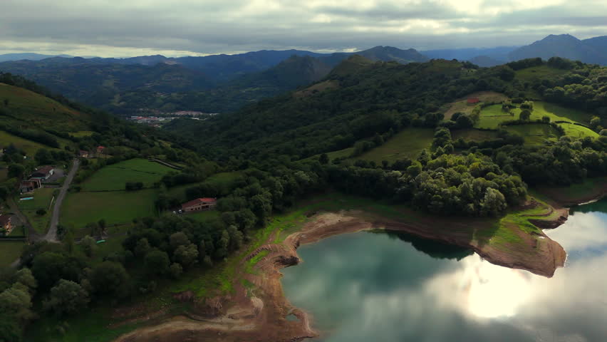 Drone view of mountain hills lake and houses under cloudy sky