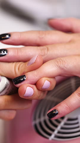 Closeup of beautician carefully applying black nail polish on fingernails of woman in beauty salon, creating perfect manicure with shiny finish