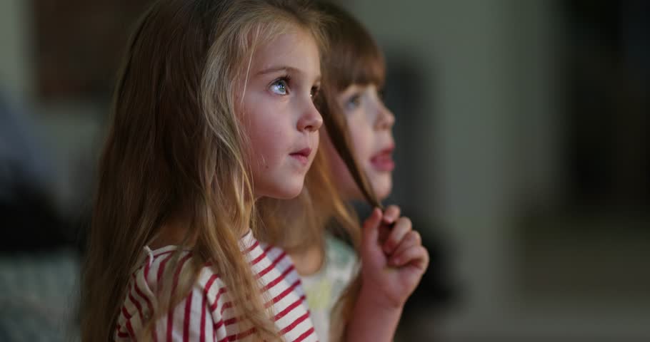 Two young girls are completely captivated by a bright screen, displaying a mix of curiosity and pure wonder