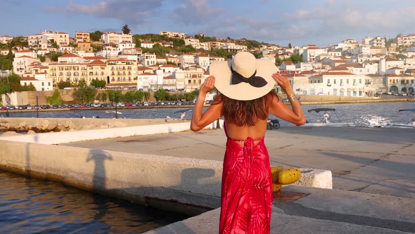 A tourist woman in a red dress looks at the town of Pylos, Messinia, Greece, during summer sunset time