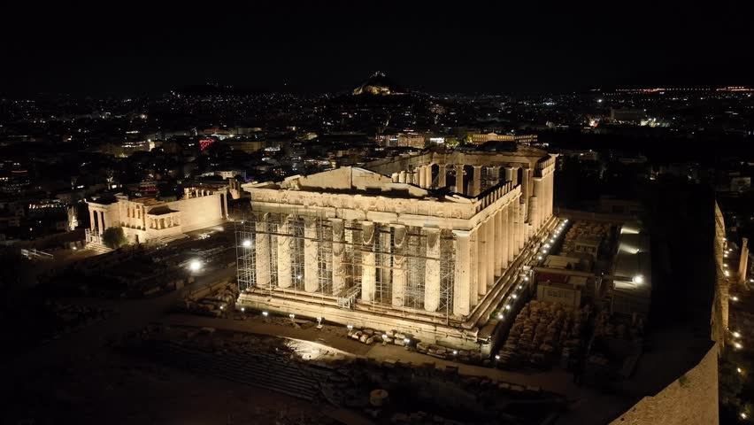 Aerial drone cinematic night video of iconic illuminated Acropolis hill and the Parthenon a world heritage landmark, Athens historic centre, Attica, Greece