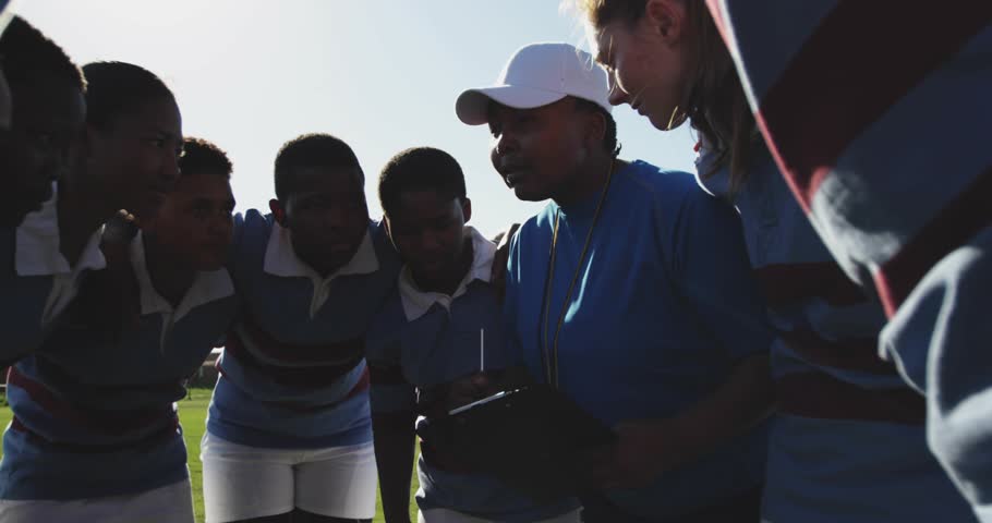 Coach with tablet addressing team pregame and sparking notifications around players stacking hands. Athletes, teamwork, fitness, sportsdecor, motivational, outdoor, energetic