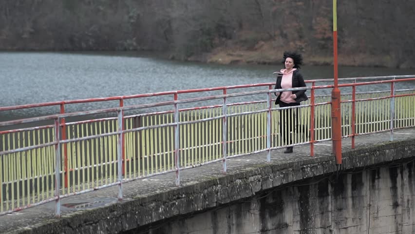 Young sportive woman jogging along a scenic riverside pathway on a cloudy day