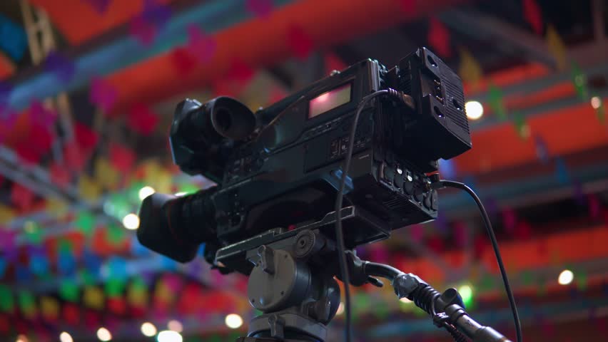 Professional video camera on a tripod filming a live show with a colorful, festive background