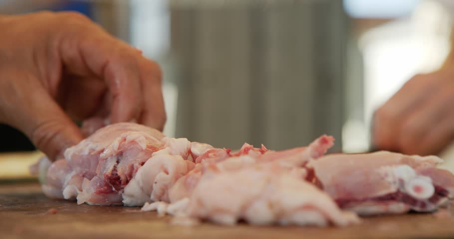 Man and woman cooking at a campsite. Close-up shot of the man cutting the chicken with a machete. A summer's day.
