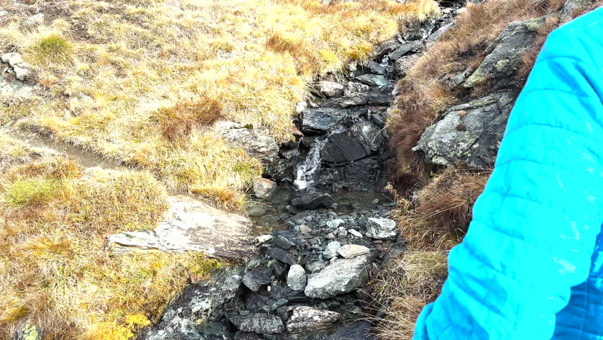 Man Hops Across Small Creek Running Over Trail in Swiss Alps