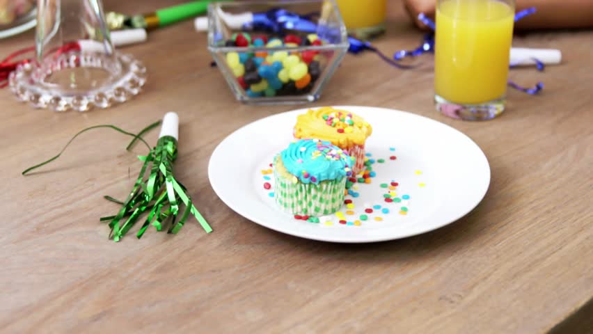 Camera opening focusing on cupcakes while confetti drifting then revealing tiered celebratory cake. Festive, celebration, dessert, tableware, colorful, cheerful, indulgent