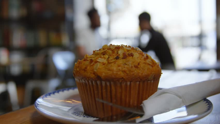Initial spark sending sugar granules falling, coating muffin as camera sliding revealing napkin. Pastry, dessert, culinary, rustic, cozy, indulgence, seasonal