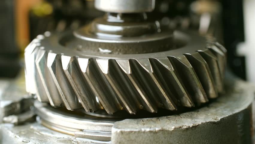 Rotating metal gear from vehicle transmission system, showing oily teeth of cogwheel in motion inside engine mechanism during its operation. Helical gear rotating inside car transmission mechanism