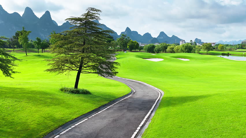 Aerial shot of a beautiful green golf course with a winding road and spectacular mountain landscape.