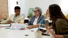 Multiethnic group of colleagues collaborating on a new business project, analyzing financial data, graphs, and pie charts during a productive discussion in a contemporary conference room - Powered by Shutterstock - Get 15% off with code: PIKWIZARD15