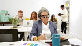 Elegant senior manager working at her desk, using a digital tablet and reviewing documents, while her diverse team collaborates in the background of a bright and contemporary open plan office - Powered by Shutterstock - Get 15% off with code: PIKWIZARD15