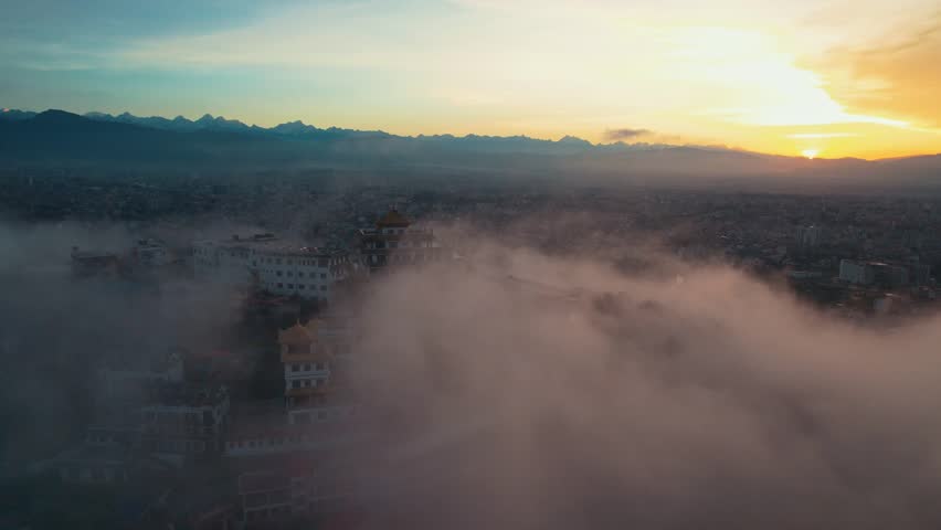 Morning aerial drone view of a Buddhist gumba in Chovar with mist, Kathmandu city, and mountains in the background