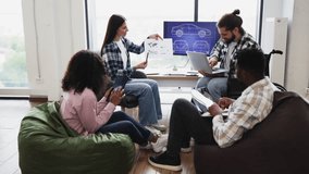Diverse group of young adults brainstorming car design. Includes man using wheelchair, women, men, different races and teamwork collaboration in open office with plans displayed on screen. - Powered by Shutterstock - Get 15% off with code: PIKWIZARD15